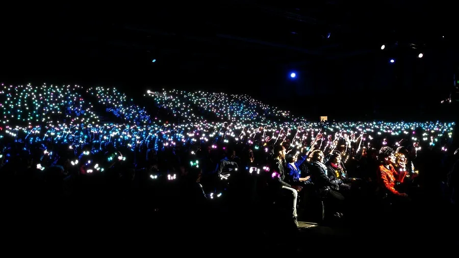 Salle de spectacle dans le noir, bracelets LED bleus allumés dans le public